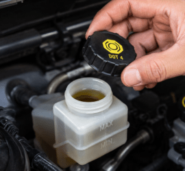 Mano abriendo el depósito de líquido de frenos DOT 4 en el motor de un coche.